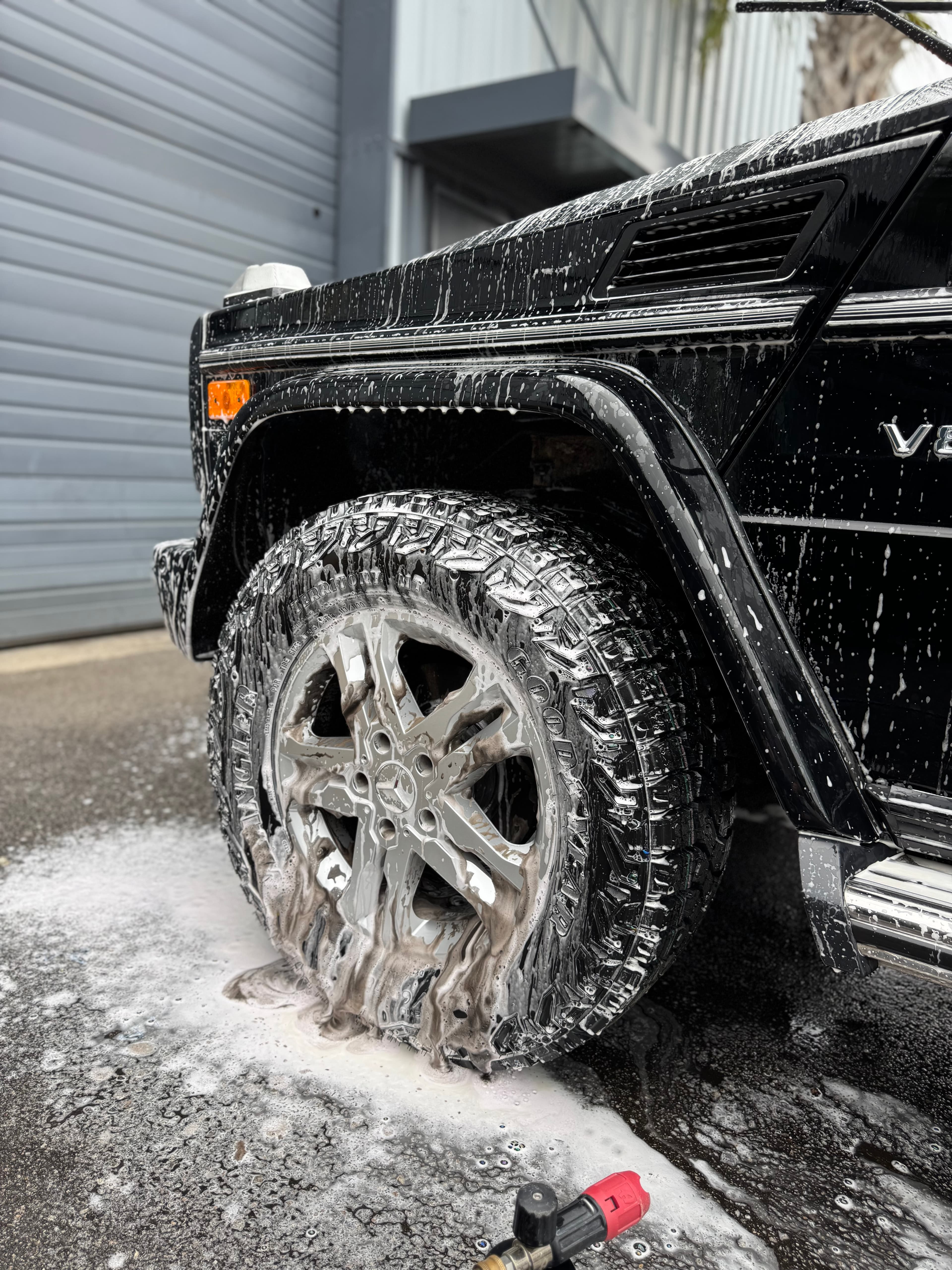 Black Mercedes G-Wagon wheel and fender covered in wash foam during detailing