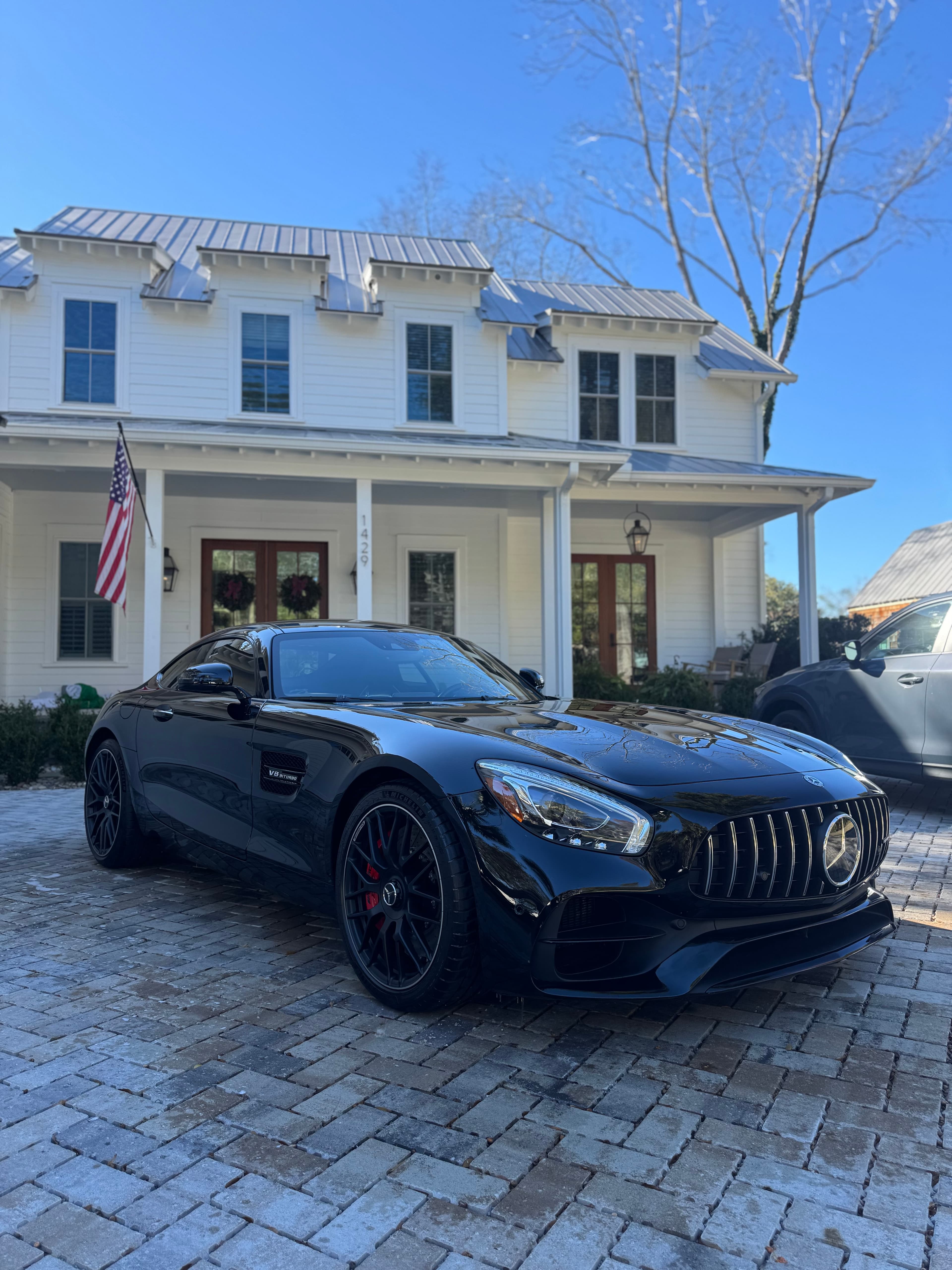 Glossy black Mercedes-AMG GT detailed in front of a white farmhouse on a sunny day