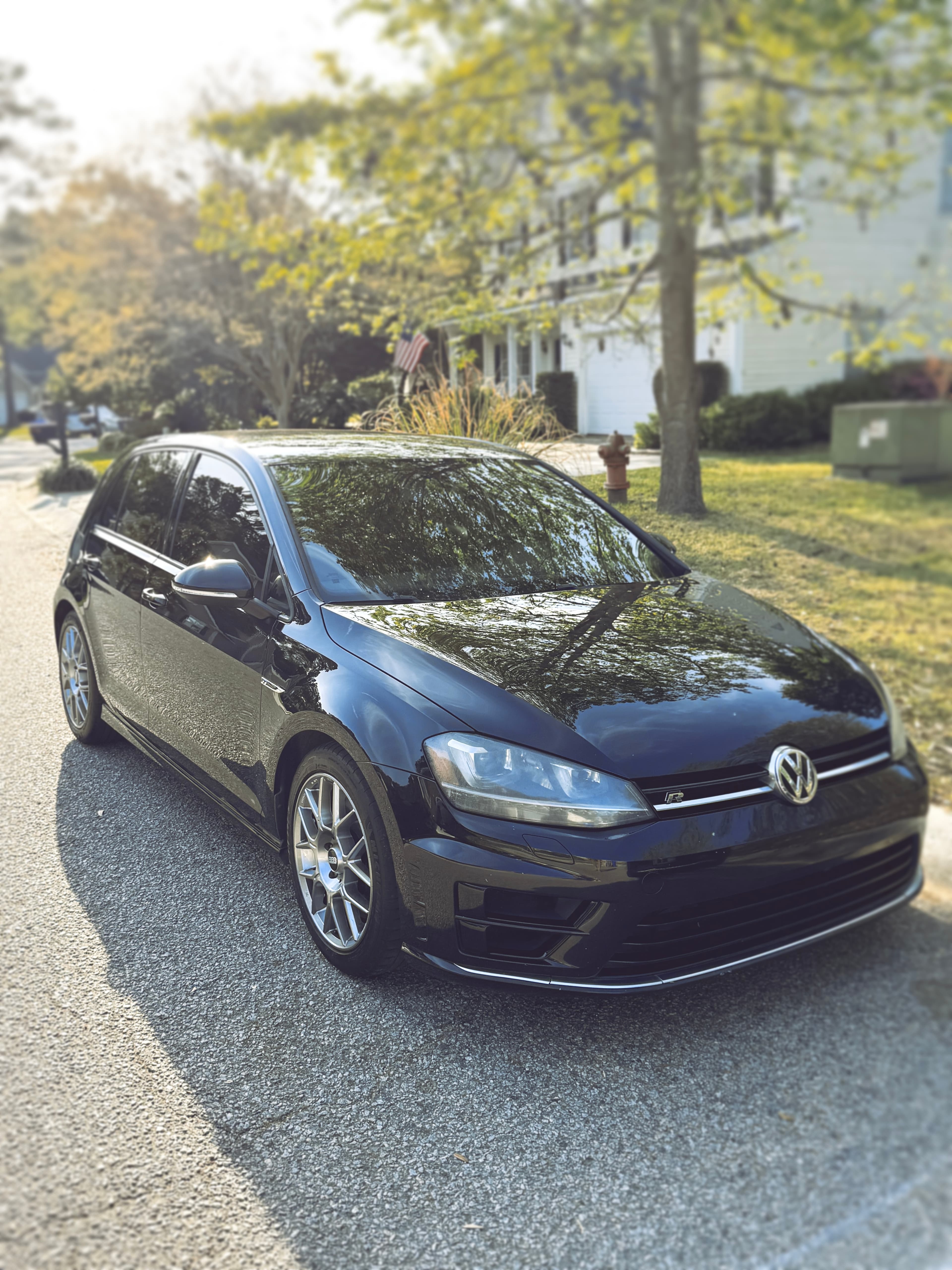 Glossy black Volkswagen Golf R detailed and parked on a tree-lined street