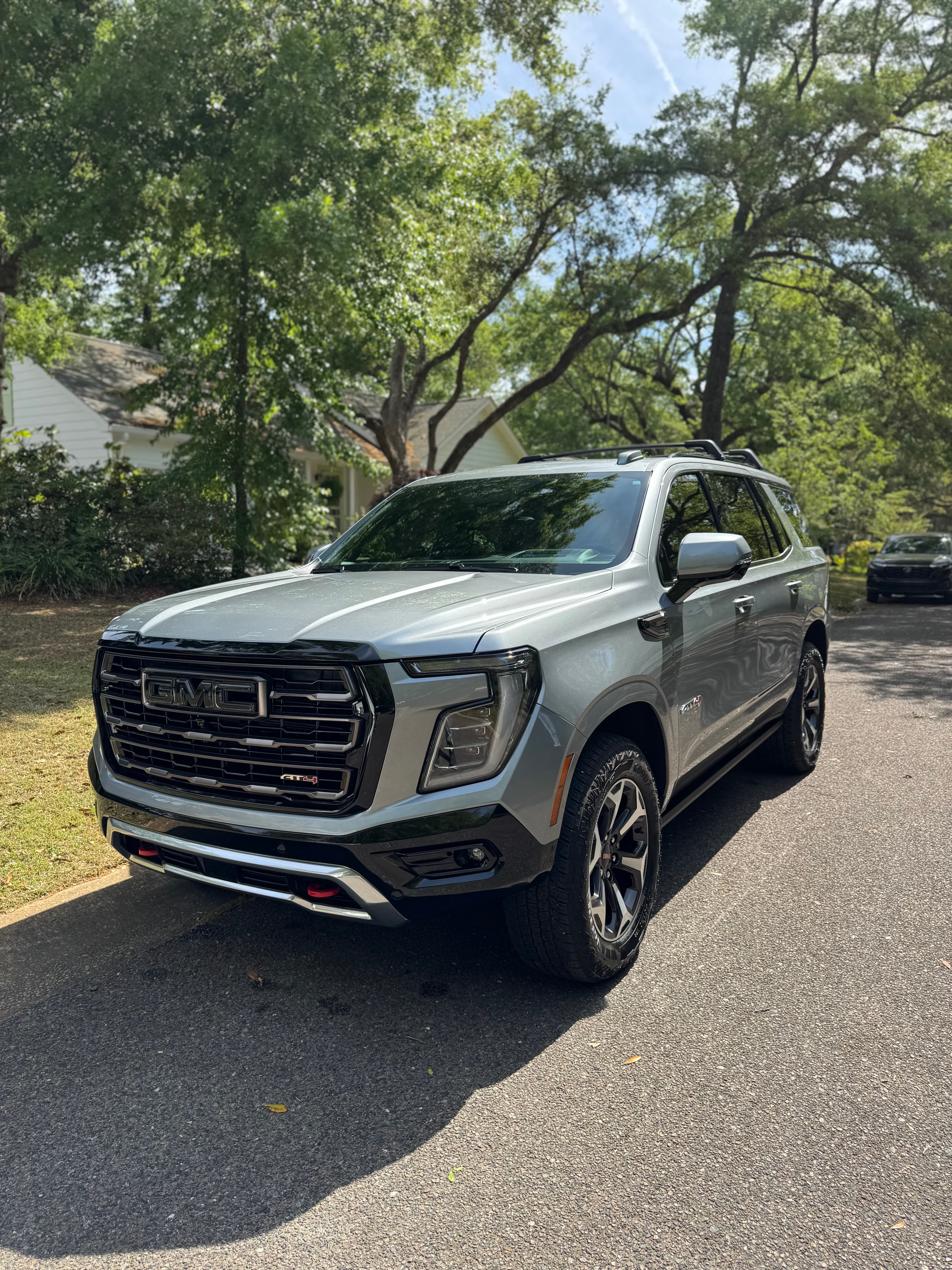 Freshly detailed silver GMC Yukon AT4 SUV, front three-quarter view on a tree-lined street